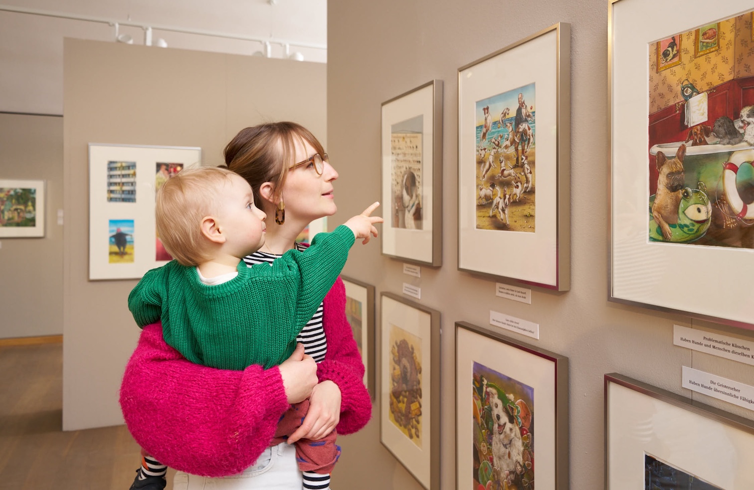 FRau mit Baby auf dem Arm. Beide schauen Bilder an der Wand an.