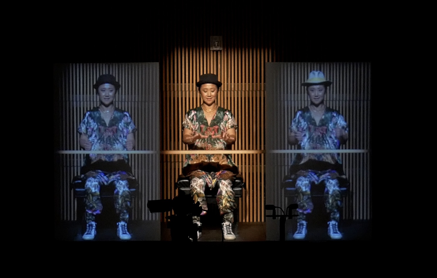 Frau mit Zylinder, jeweils rechts und lins von ih wird ein Bild von ihr an die Wand projiziert